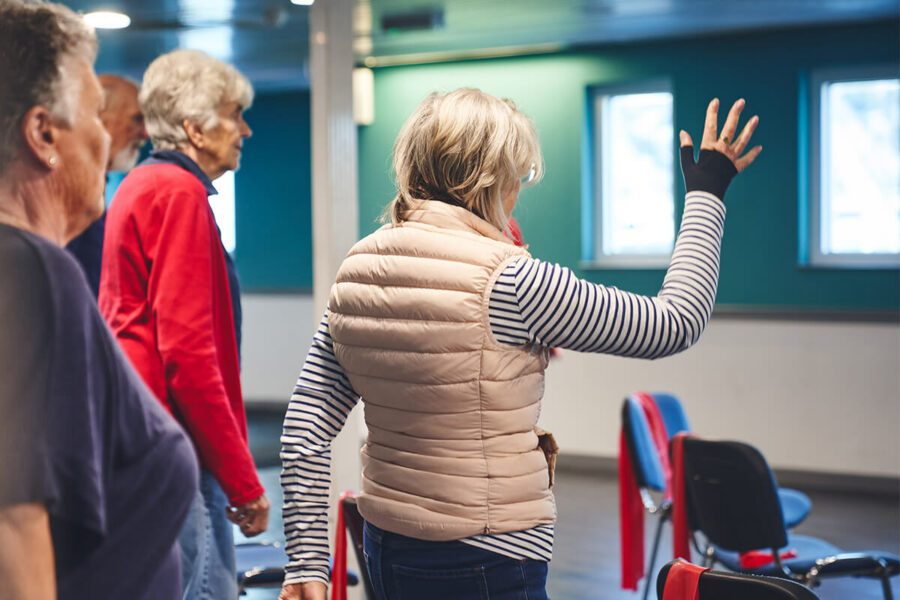 An older lady participant follows an instructor with gentle standing exercises at an iCareiMove mobility and falls prevention class.