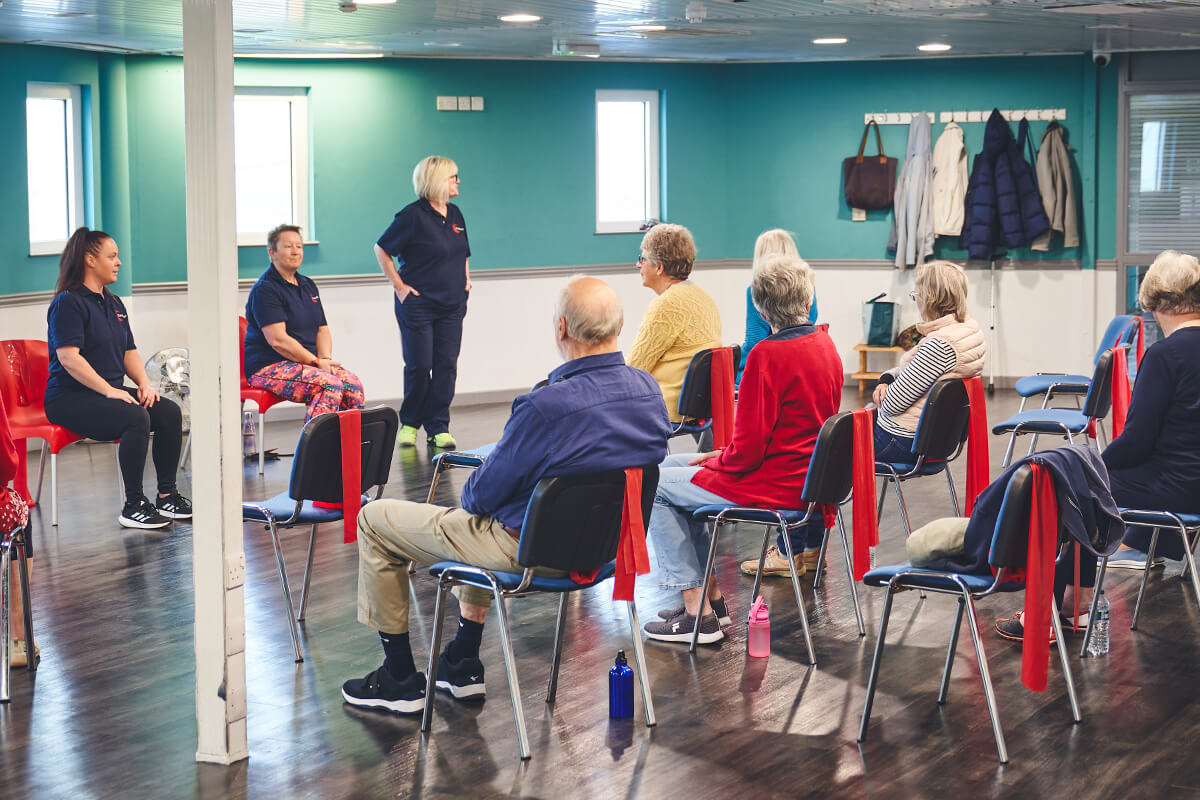 Three iCareiMove instructors lead a seated group exercise class with older participants.