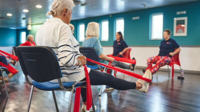An older participant uses resistance bands for gentle seated exercise activities at an Impact falls prevention event.