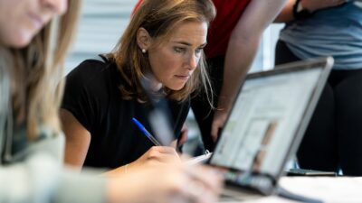 A young female fitness professional studies closely in a group with other people in a professional office setting.