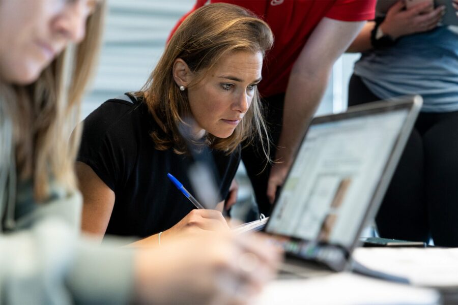 A young female fitness professional studies closely in a group with other people in a professional office setting.