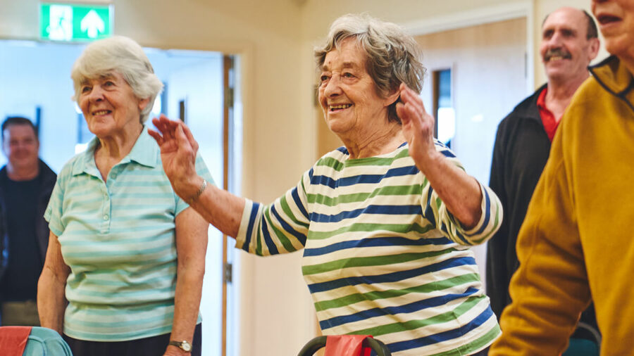 A happy older woman participating in standing mobility and falls prevention exercises.