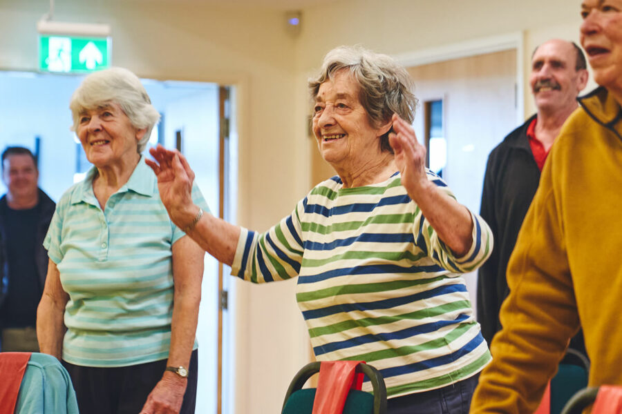 A happy older woman participating in standing mobility and falls prevention exercises.