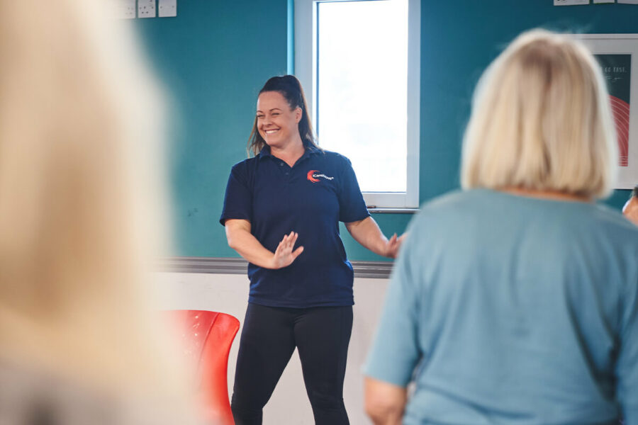 A happy iCareiMove instructor leads a gentle falls prevention exercise class for older people.