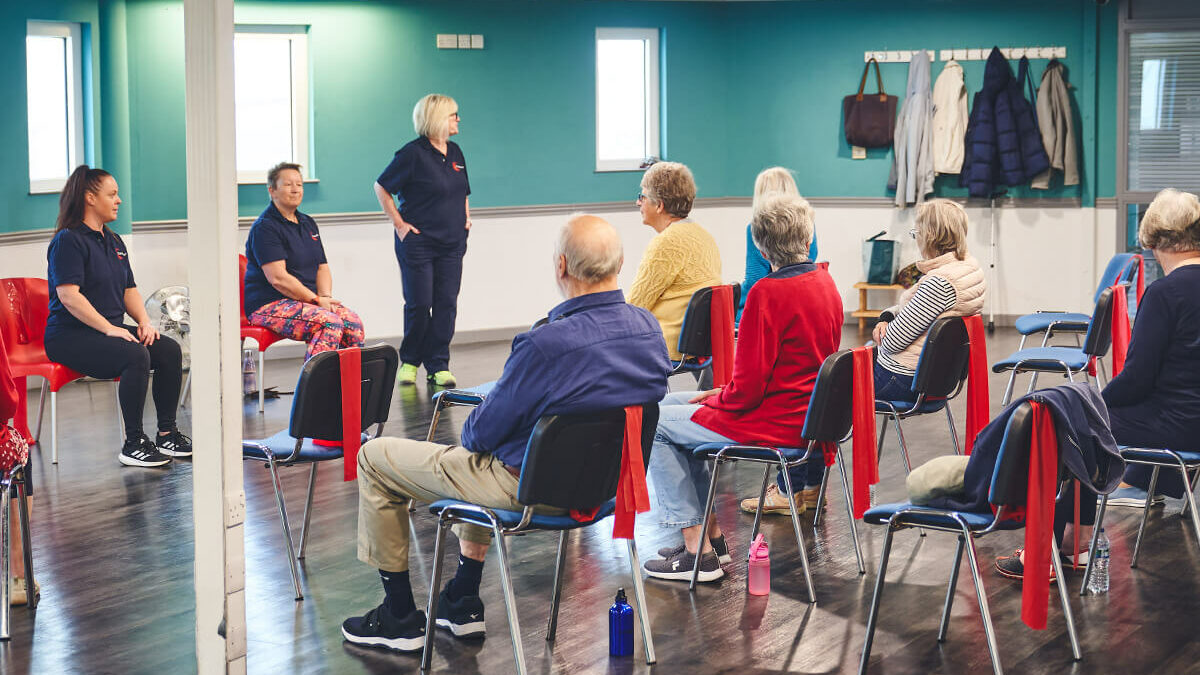 Three iCareiMove instructors lead a seated group exercise class with older participants.