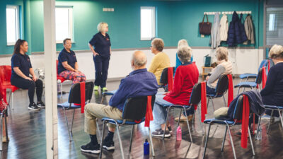 Three iCareiMove instructors lead a seated group exercise class with older participants.