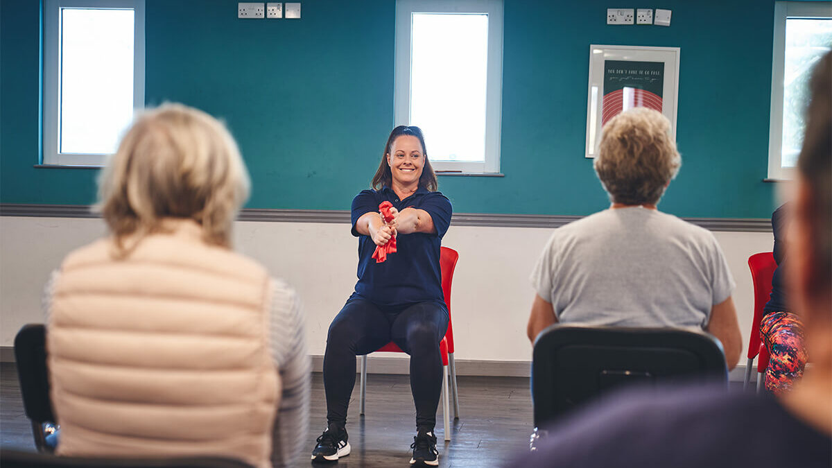 An iCareiMove Instructor leads gentle seated exercise activities for grip strength at an Impact falls prevention event.