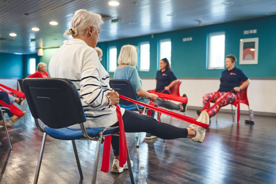 An older participant uses resistance bands for gentle seated exercise activities at an Impact falls prevention event.