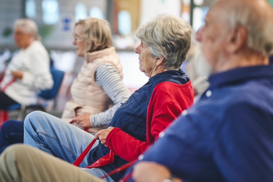 An older participant uses resistance bands for gentle seated exercise activities at an Impact falls prevention event.